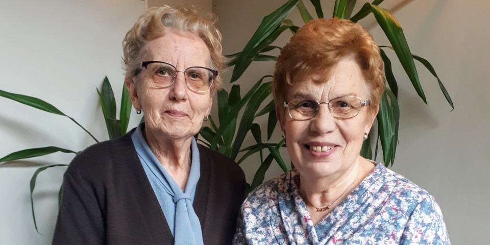 Agnes en Lucie doen samen mee aan de leesgroep van OKRA Sint-Willibrordus. Ze lachen en kijken in de lens en hebben het boek 'Mazzel Tov' in handen.